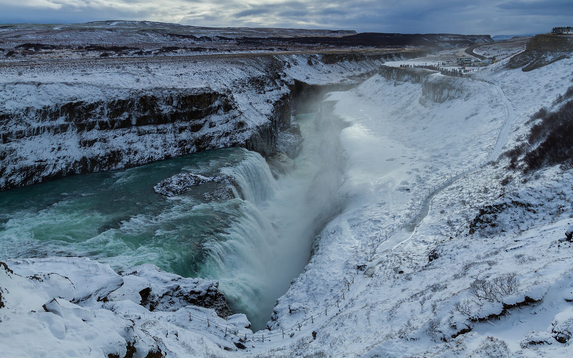 Gullfoss waterfall in winter, white water dropping between dark rock walls covered with snow.