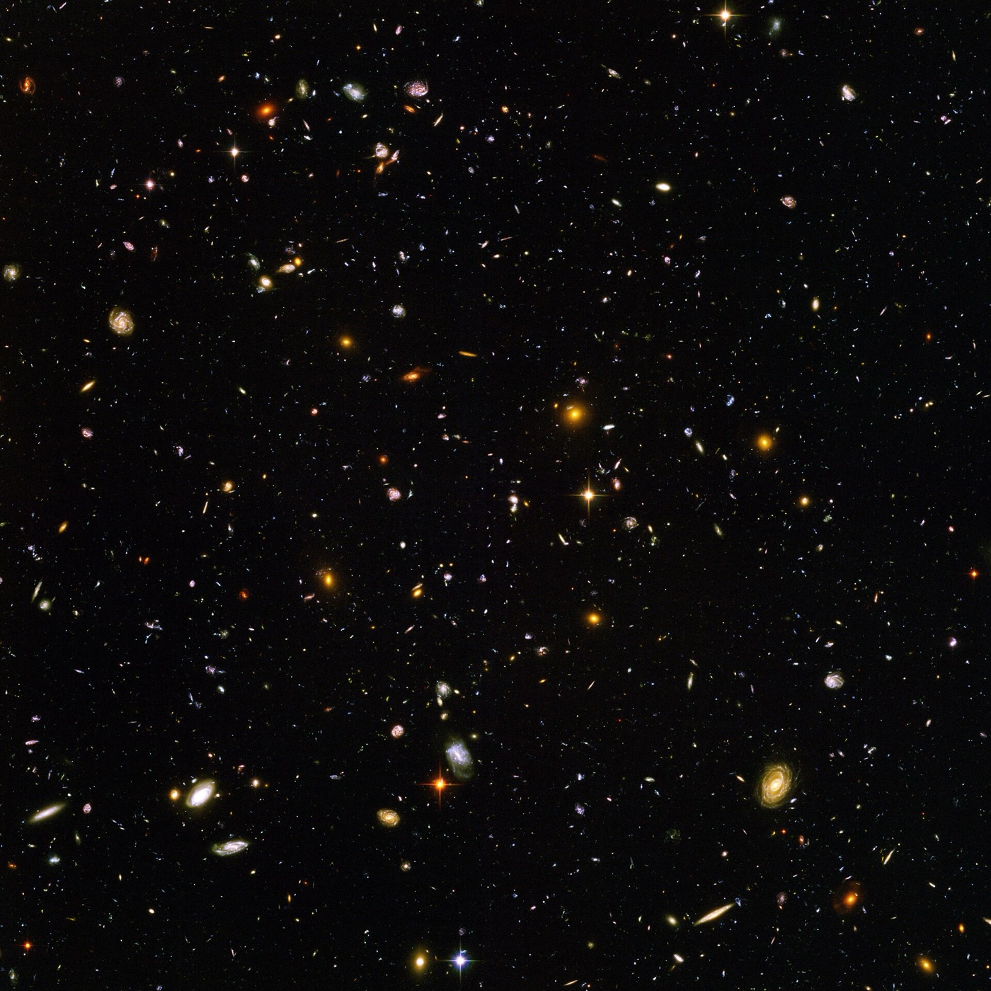 The Hubble Ultra Deep Field: thousands of distant galaxies scattered across black space, with a few bright foreground stars.