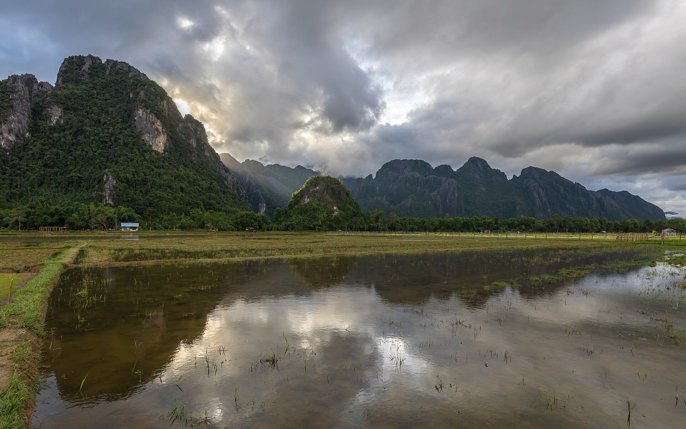 Karst mountains in Vang Vieng, Laos, with shafts of evening light falling through clouds onto flooded rice fields.